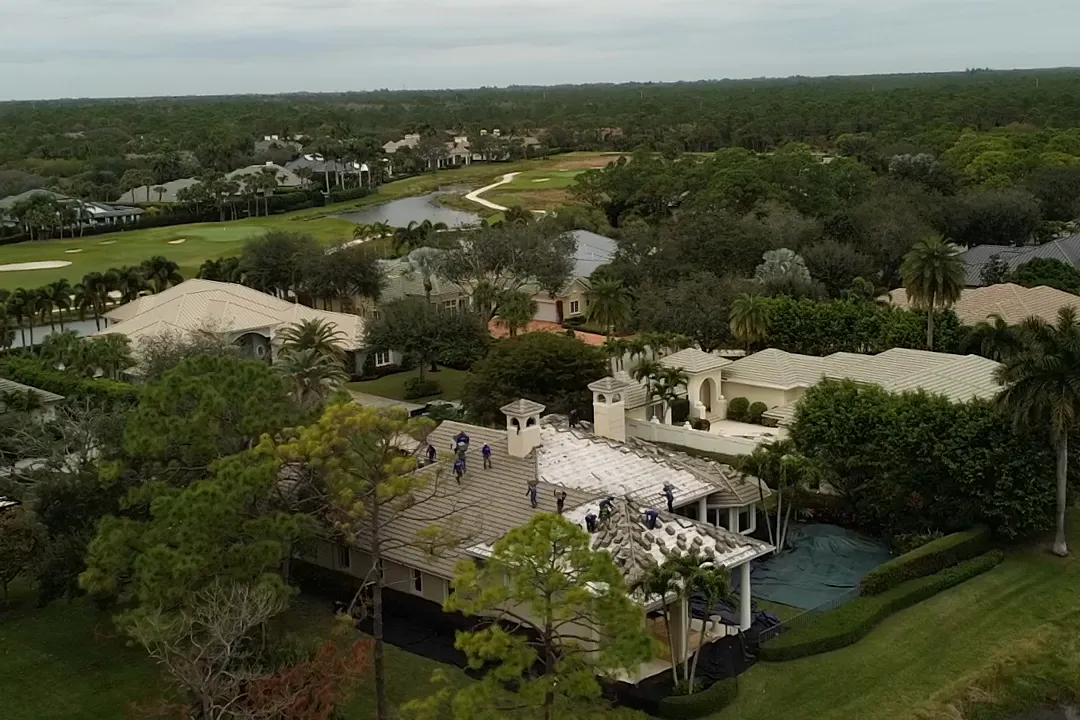 A drone view over golf course homes in West Palm Beach, a roof under replacement by the water