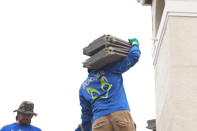 A roofer carrying a stack of tiles up to the roof on a West Palm Beach job