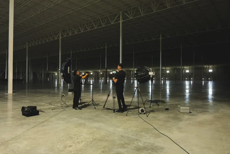 Our crew lighting a set in an empty warehouse, two cameras and soft boxes on stands