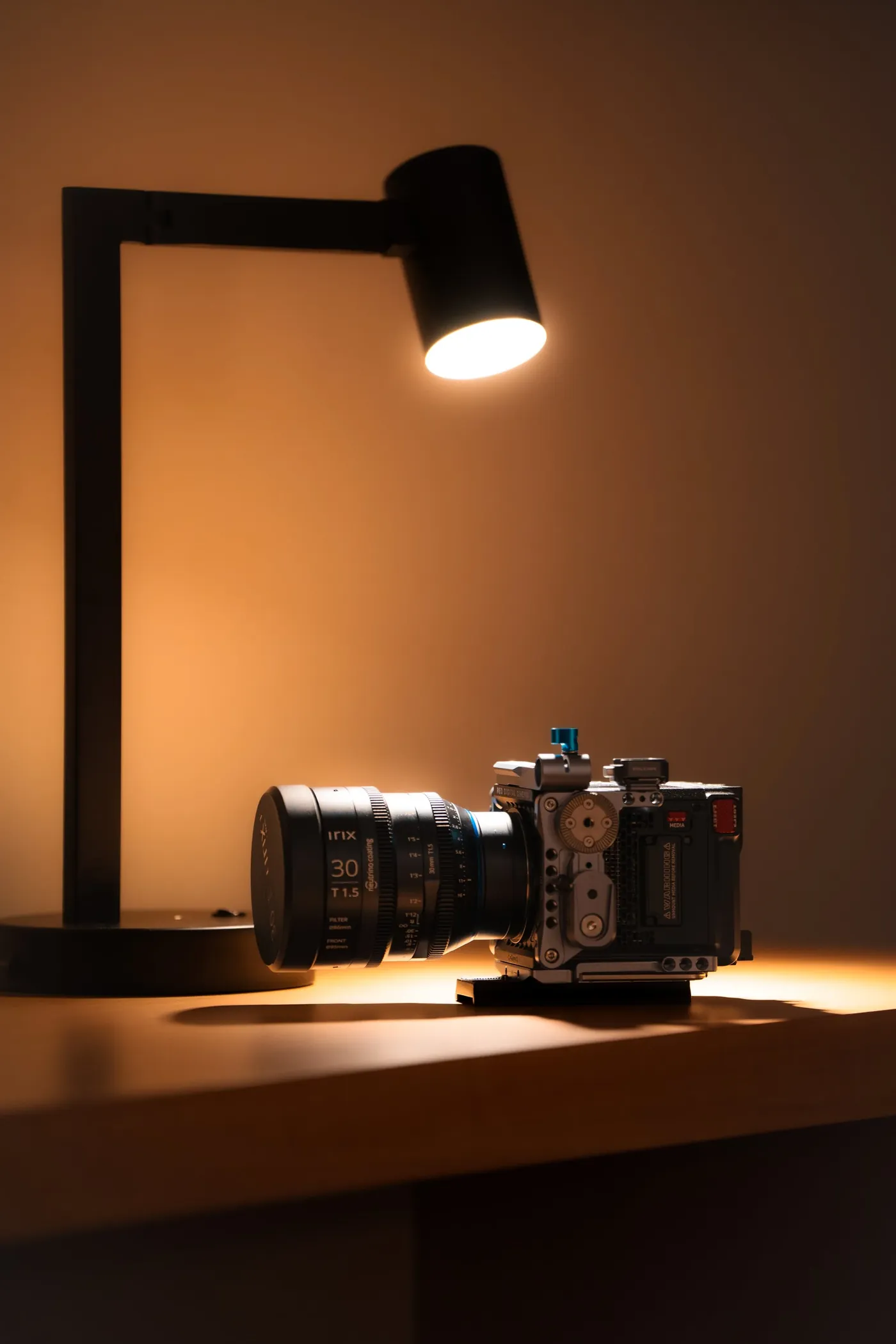 A cinema camera on a desk under a warm lamp