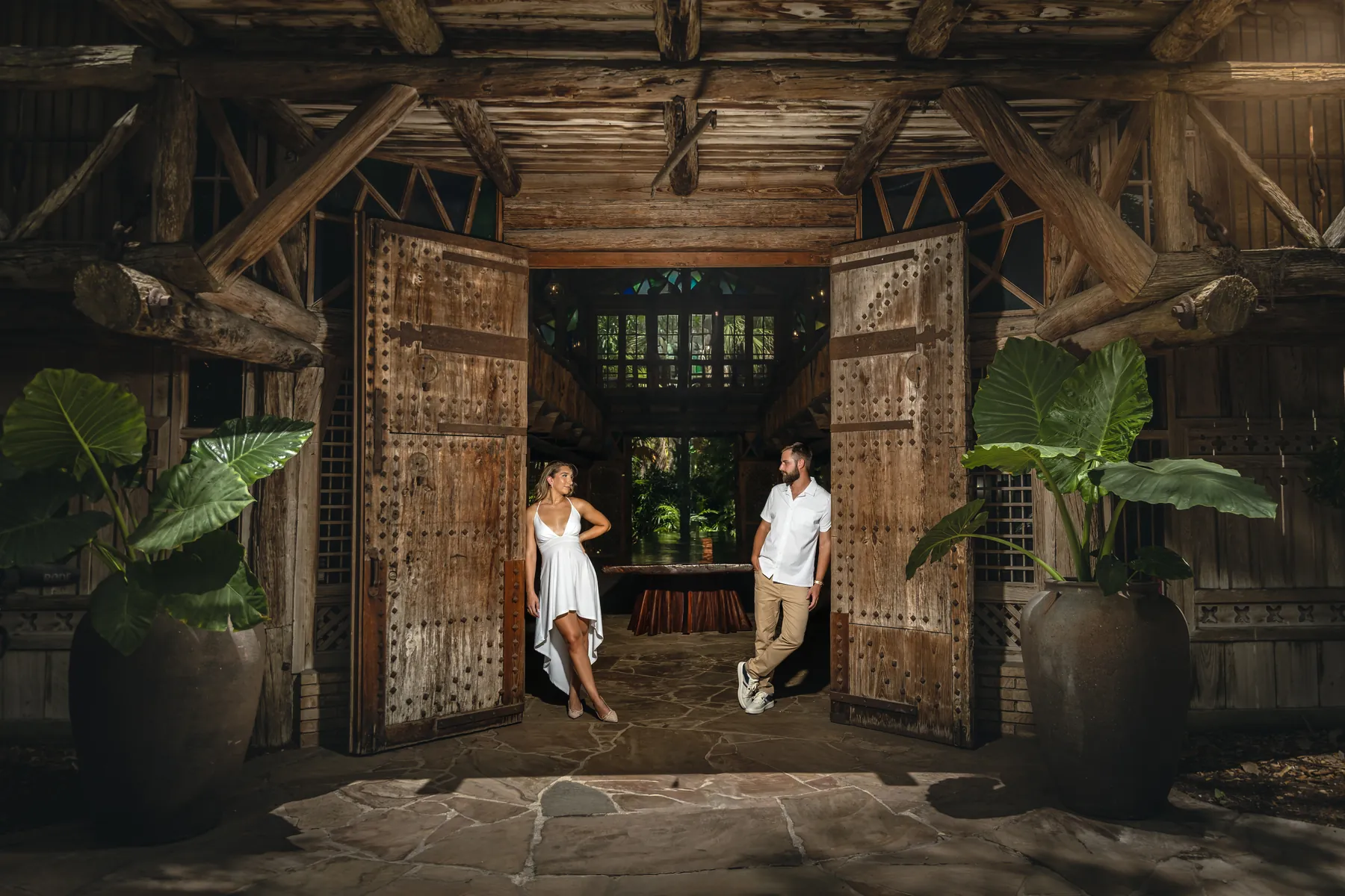 A couple standing in a tall carved wooden doorway framed by large tropical plants