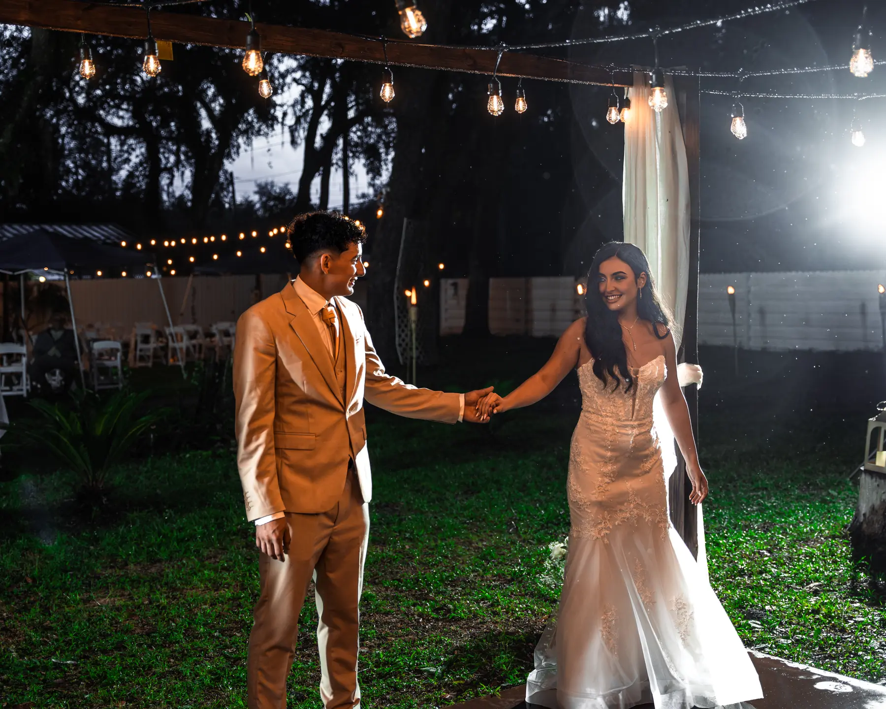 A couple holding hands on an outdoor dance floor at night under strings of lights