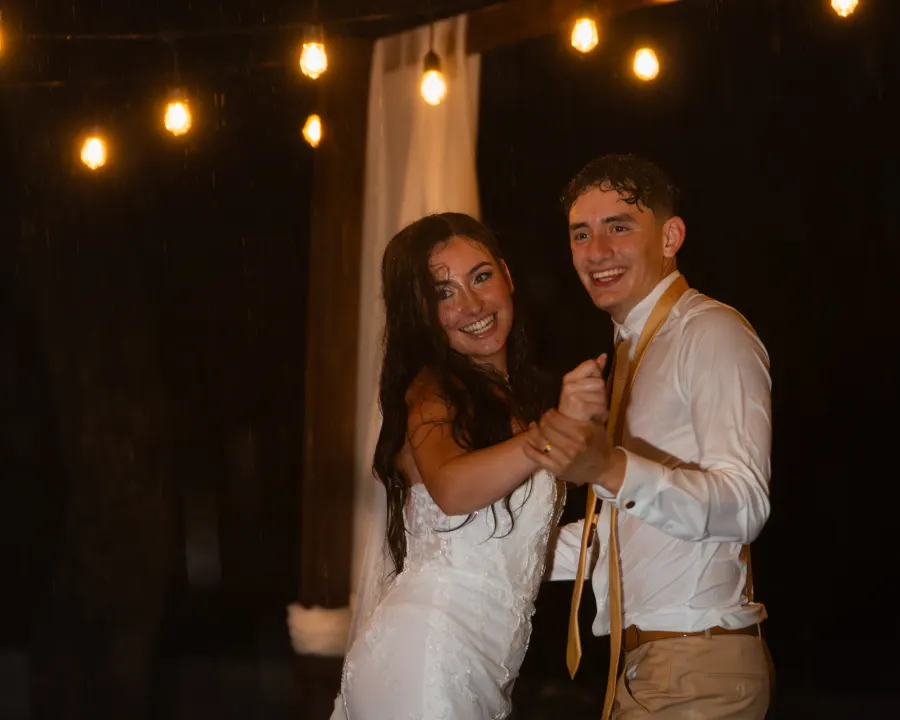 The bride and groom laughing as they dance under strings of warm lights at night