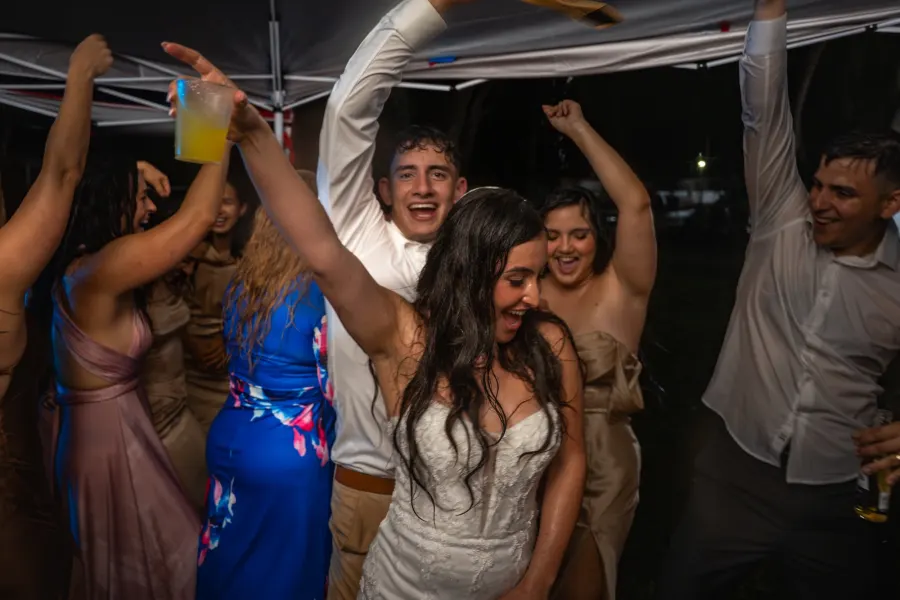 The bride dancing with her arms up in a crowd of friends and family under a party tent
