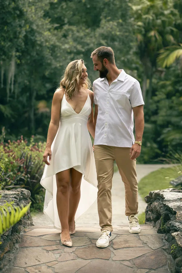 A couple in white walking hand in hand toward the camera on a stone garden path