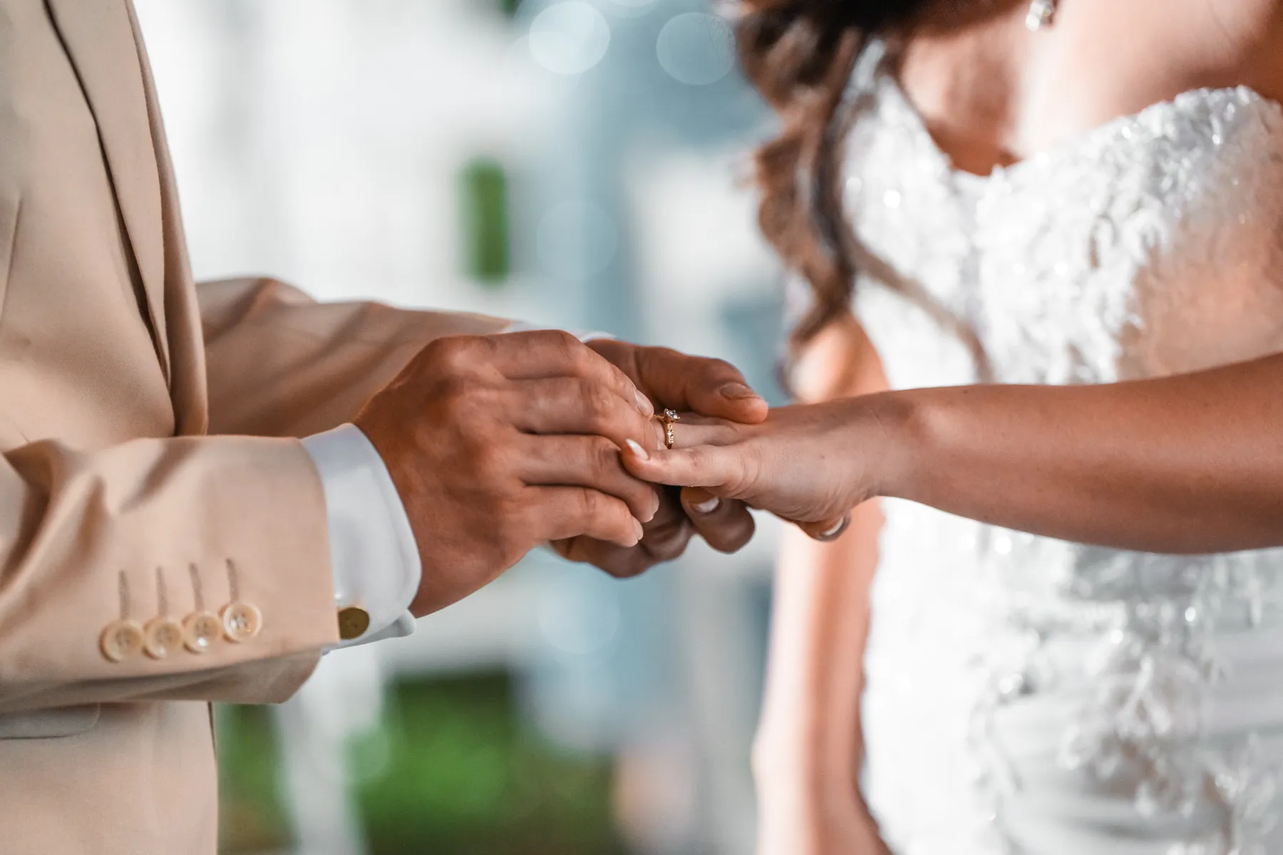 Close up of a groom in a tan suit sliding a ring onto the bride's finger