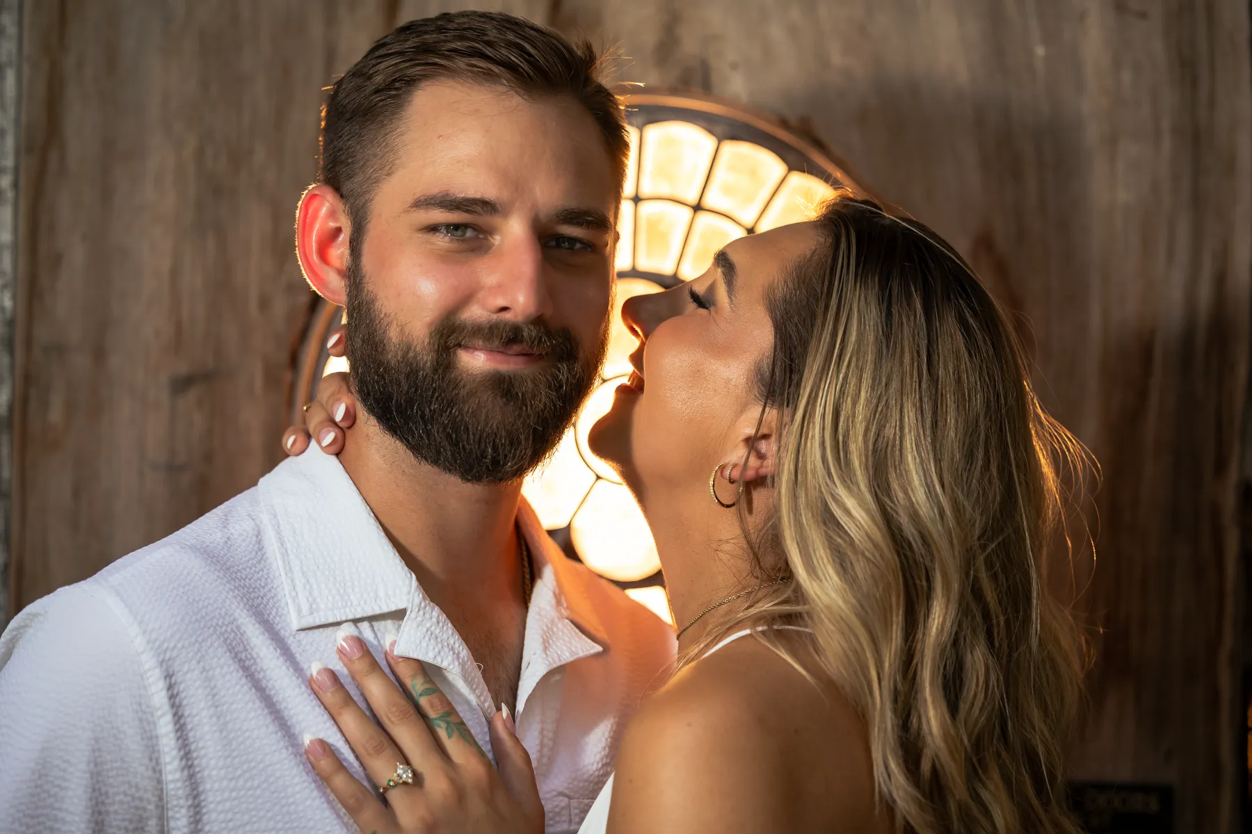 Close up of a couple in front of a round stained glass window, her hand with the ring resting on his chest