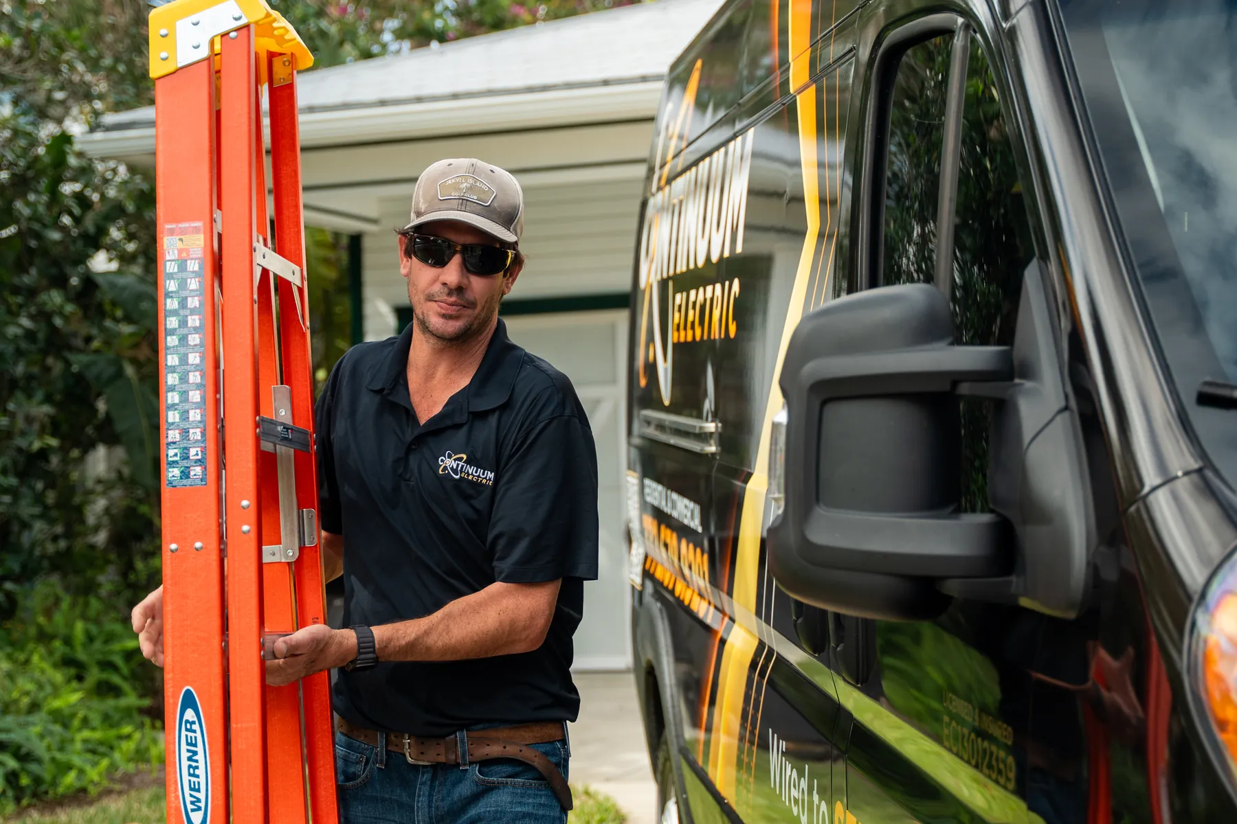 An electrician carrying an orange ladder off the van