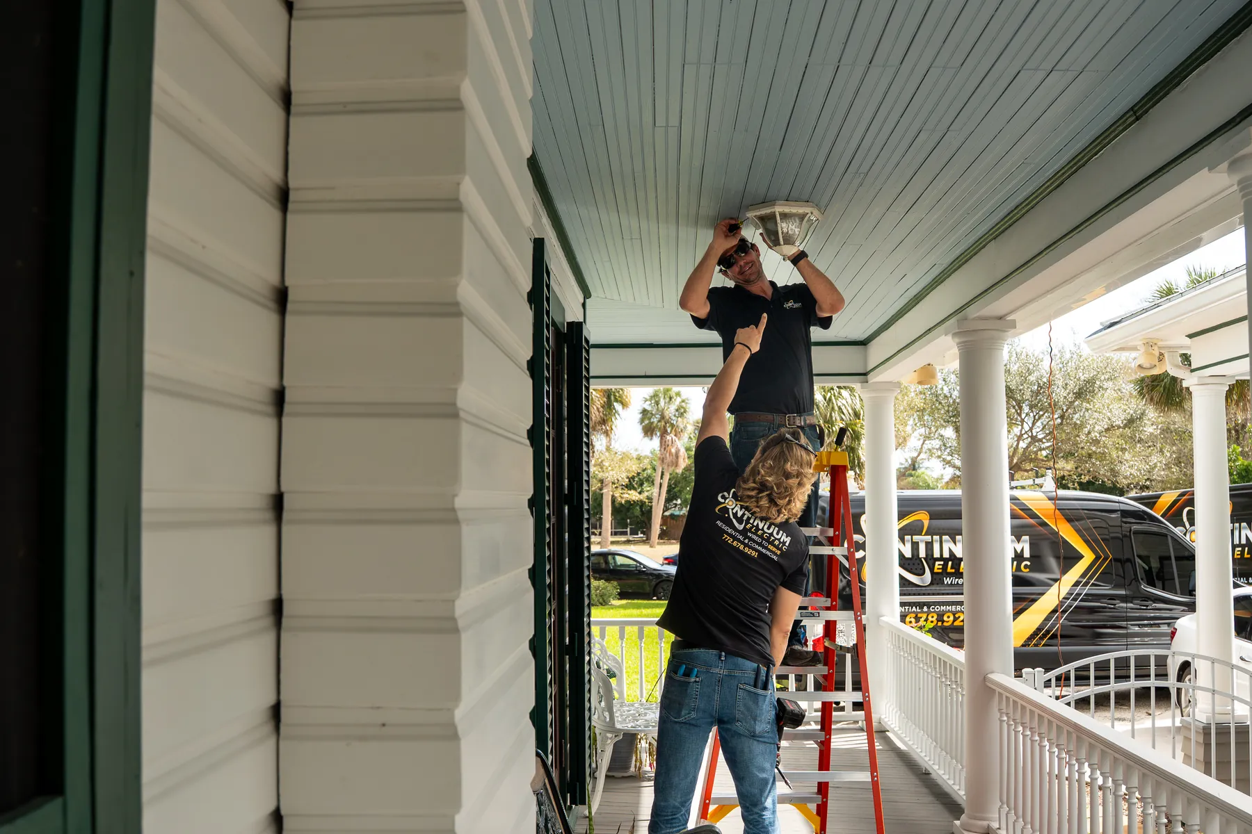 Two electricians replacing a porch light on a white house
