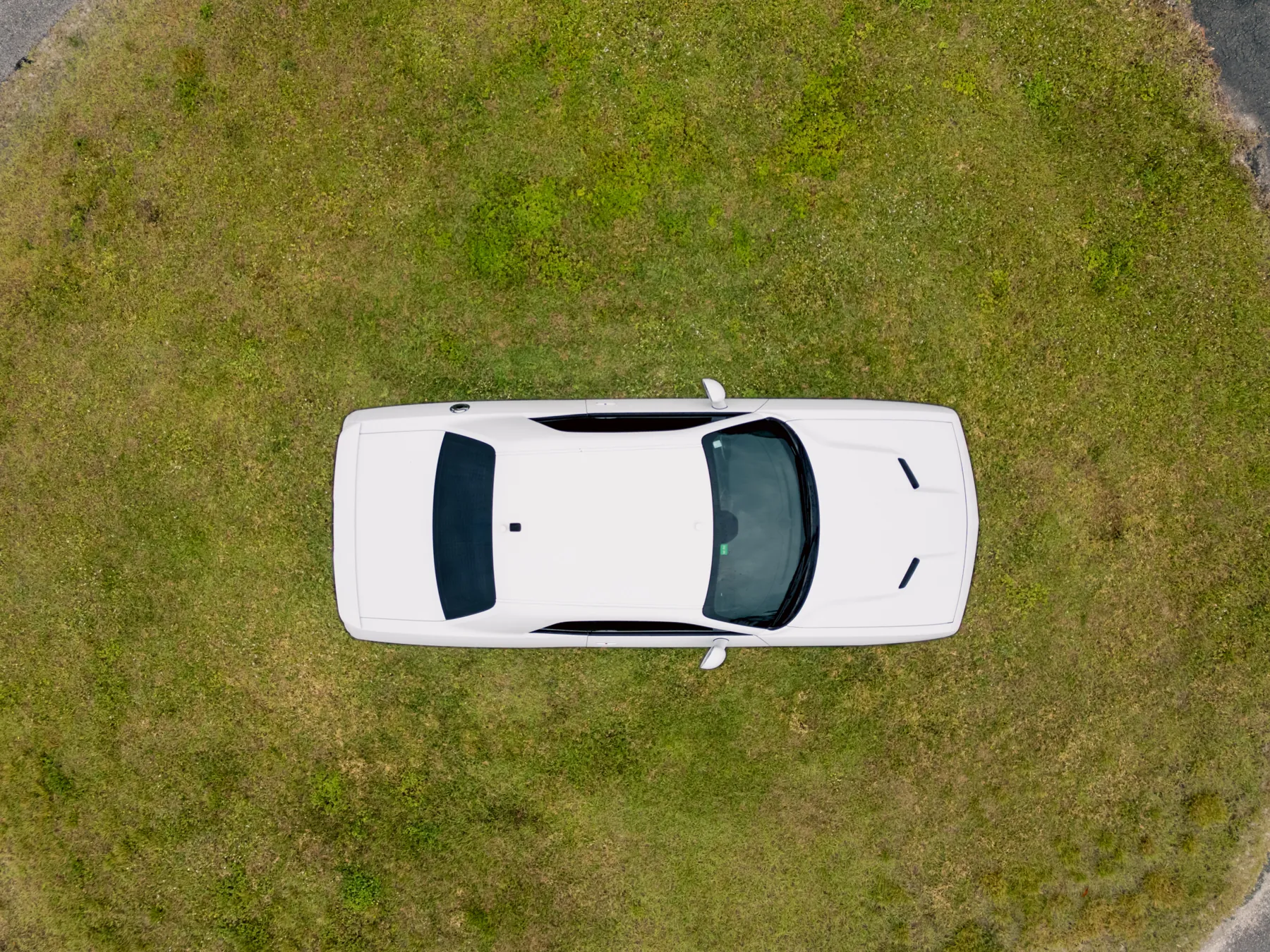 Drone view straight down on a white car parked inside a ring of grass