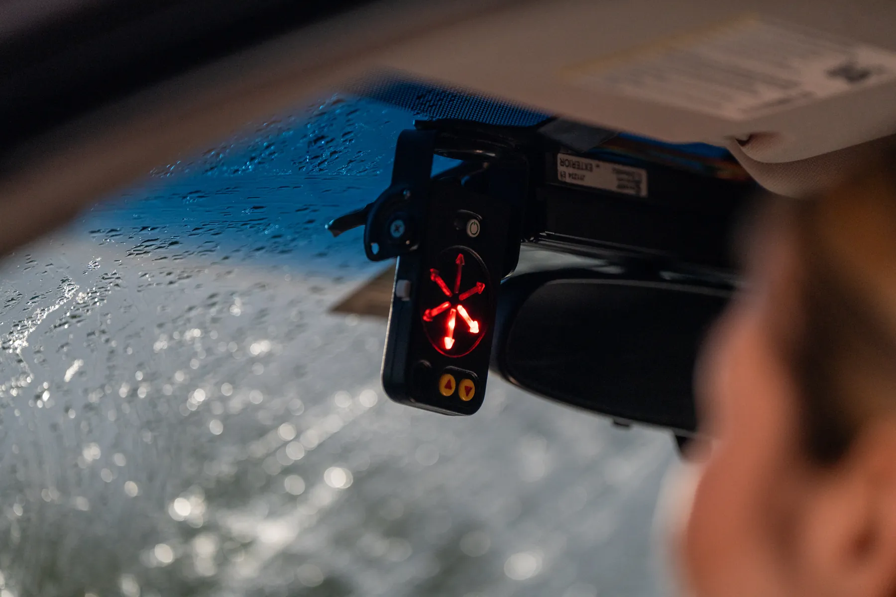 The StopAmbush display under the sun visor glowing red, rain on the windshield behind it